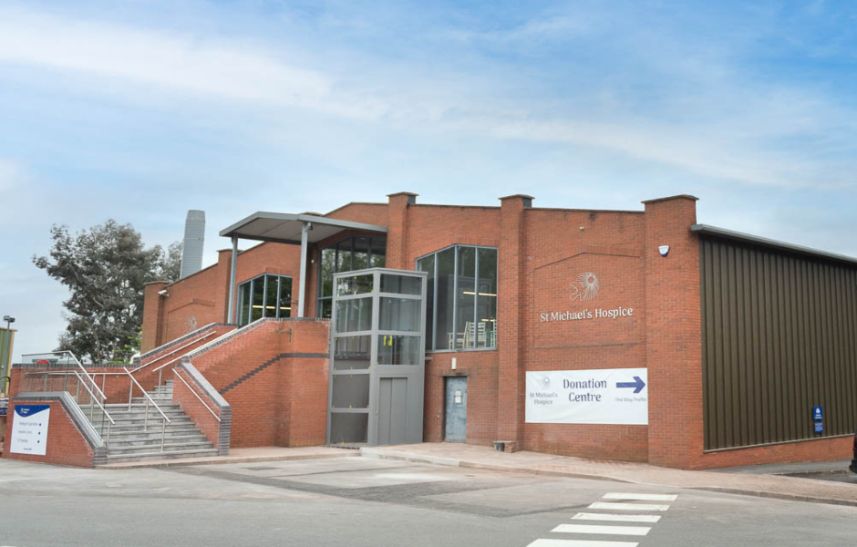 View of two story large red brick building with stairs and lift at front.