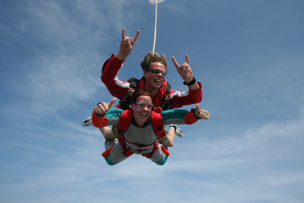 Two men taking part in a tandem skydive freefalling with thumbs up