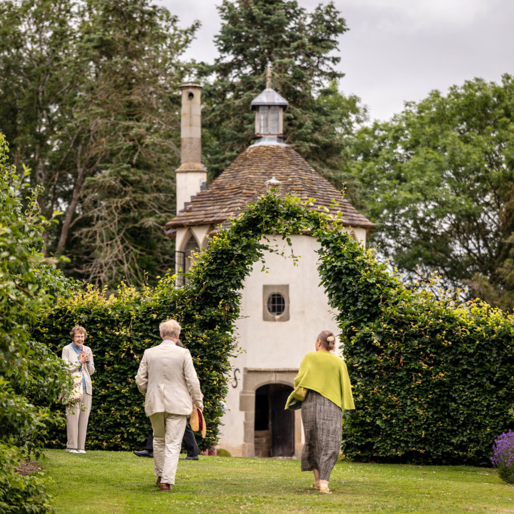 A couple strolling through a serene garden, hand in hand, surrounded by colorful flowers and lush greenery.