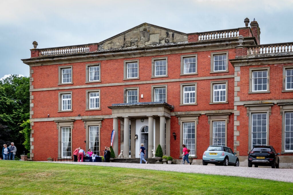 A bustling scene outside a massive red brick building, with people gathered around, creating a lively atmosphere.