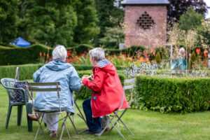 Two elderly individuals enjoying each other's company while sitting at a table in a serene garden setting.