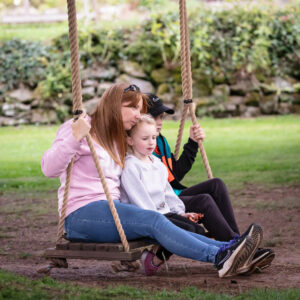 A woman and two children happily swinging together in a park.