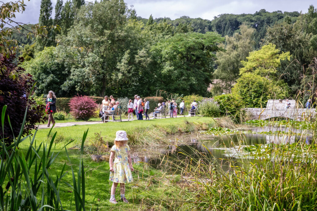 A young girl in a dress strolling by a pond on a path.