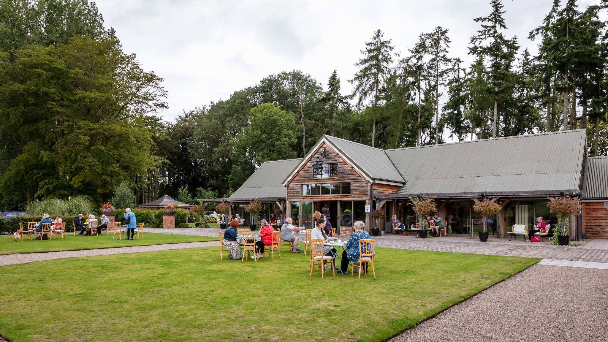 People sitting at tables in a garden with a large building in the background.