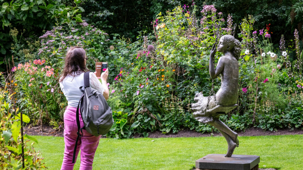 A woman capturing a photo of a garden statue.