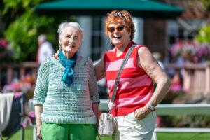 Two elderly women standing side by side on a green field.