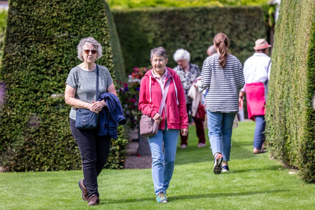 A serene garden with people strolling amidst hedges and trees, creating a peaceful and natural ambiance.