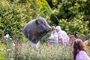 People admiring a bull statue amidst a vibrant flower garden.