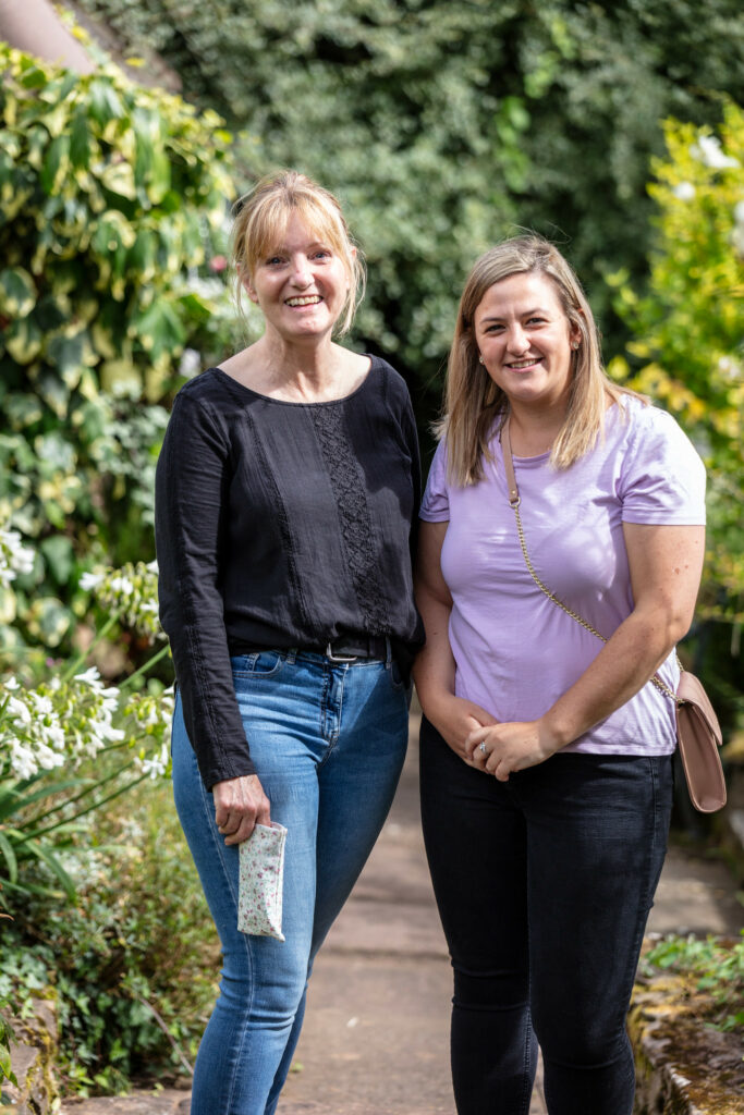 Two women standing in a garden surrounded by lush plants and flowers.