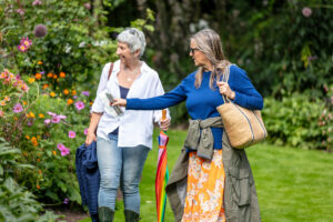 Two women strolling in a garden, each holding an umbrella to shield themselves from the rain.