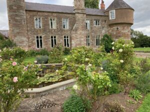 A picturesque castle surrounded by a serene pond and blooming roses in the foreground.