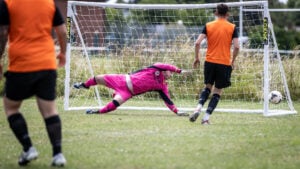 Male goalkeeper diving onto the pitch to save a goal