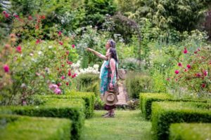 A man and woman standing in a garden, surrounded by colorful flowers and lush greenery.