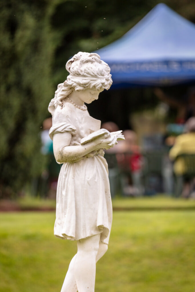 A statue of a girl engrossed in a book, placed in a serene park setting.