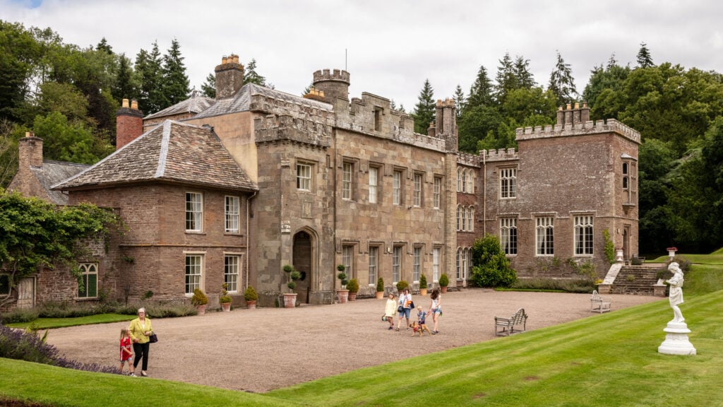 People walking around a stone building in a lush green field.