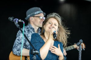 A woman singing into a microphone while a man plays guitar on stage.