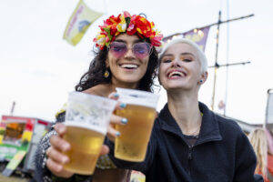 Two women enjoying beer at a festival, smiling and holding glasses.