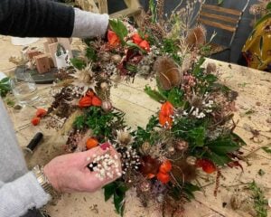 Two hands arranging dried flowers on a wreath atop a wooden table